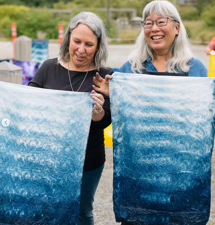 Two women holding large blue and white patterned fabric outdoors.